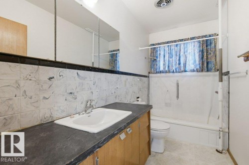 Bathroom with a vanity featuring a white drop-in sink, an extended countertop, and wood-finish cabinetry - 10459 66 Avenue Nw, Edmonton, AB - Indoor Photo Showing Bathroom