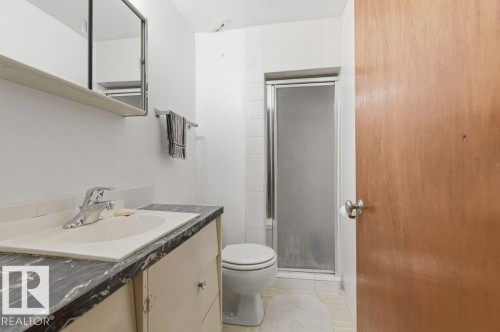 Bathroom featuring a vanity with an integrated sink, a dark patterned countertop, a wall-mounted mirror, a toilet, and a glass-enclosed shower - 10459 66 Avenue Nw, Edmonton, AB - Indoor Photo Showing Bathroom