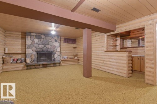 Spacious room featuring log-style paneling, a stone fireplace, integrated shelving, and a built-in wet bar with wood cabinetry - 10459 66 Avenue Nw, Edmonton, AB - Indoor With Fireplace