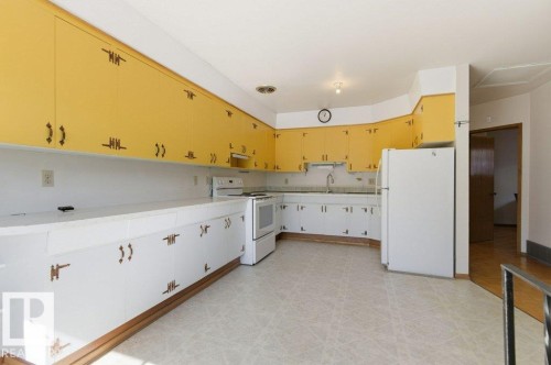 Kitchen featuring extensive upper yellow cabinetry and lower white cabinetry with decorative hardware, white countertops, and white appliances - 10459 66 Avenue Nw, Edmonton, AB - Indoor Photo Showing Kitchen
