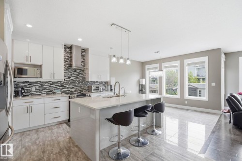 Contemporary kitchen featuring a large center island with seating, white shaker cabinetry, stainless steel appliances, and a mosaic tile backsplash - 1051 174 Street Sw, Edmonton, AB - Indoor Photo Showing Kitchen With Upgraded Kitchen