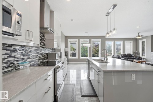 Modern kitchen featuring white cabinetry, a tiled backsplash, stainless steel appliances, an integrated range hood, and an oversized island with a built-in sink and pendant lighting - 1051 174 Street Sw, Edmonton, AB - Indoor Photo Showing Kitchen With Double Sink With Upgraded Kitchen