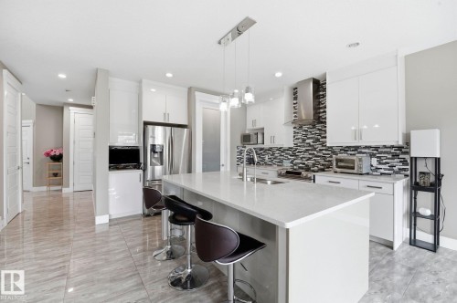 Modern kitchen featuring a large center island with integrated sink, stainless steel appliances, white cabinetry, and a monochrome mosaic tile backsplash - 1051 174 Street Sw, Edmonton, AB - Indoor Photo Showing Kitchen With Upgraded Kitchen