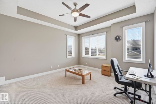 Spacious room featuring a tray ceiling with a ceiling fan, abundant natural light from multiple windows with blinds, and neutral carpet flooring - 1051 174 Street Sw, Edmonton, AB - Indoor Photo Showing Office