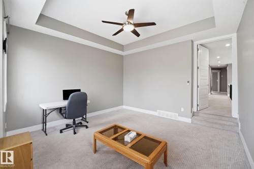 Spacious room featuring a tray ceiling, ceiling fan with integrated lighting, light gray wall finishes, white baseboards, and neutral-toned carpeting - 1051 174 Street Sw, Edmonton, AB - Indoor