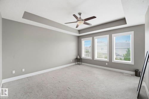 Spacious room featuring a tray ceiling, ceiling fan with integrated lighting, and three large windows with white trim - 1051 174 Street Sw, Edmonton, AB - Indoor Photo Showing Other Room