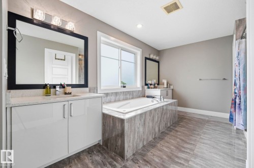 Bathroom featuring a built-in soaking tub with a tiled surround, dual vanity with light countertops, contemporary cabinetry, and large format floor tiling - 1051 174 Street Sw, Edmonton, AB - Indoor Photo Showing Bathroom