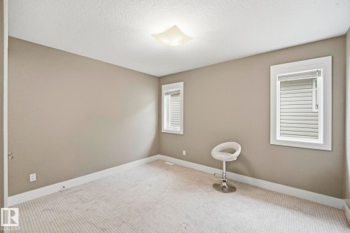 Carpeted room featuring two windows with blinds, a neutral wall color, white trim, and a ceiling-mounted light fixture - 1051 174 Street Sw, Edmonton, AB - Indoor Photo Showing Other Room