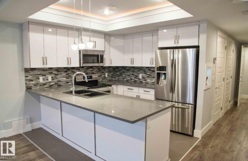 Contemporary kitchen featuring white cabinetry, stainless steel appliances, a mosaic tile backsplash, and an island with a double sink - 1051 174 Street Sw, Edmonton, AB - Indoor Photo Showing Kitchen With Double Sink With Upgraded Kitchen