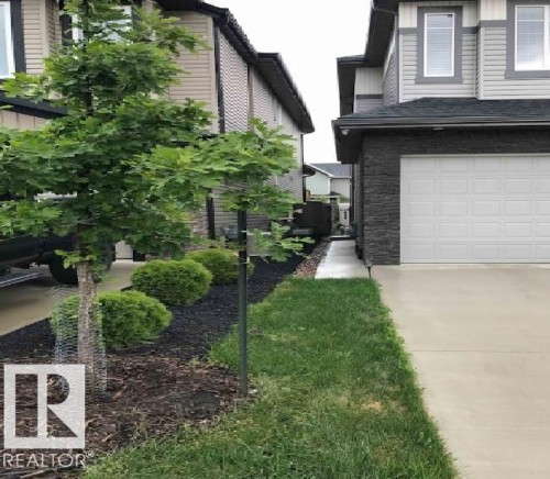 Garage exterior featuring stacked stone accents, horizontal siding, and a paneled garage door - 1051 174 Street Sw, Edmonton, AB - Outdoor
