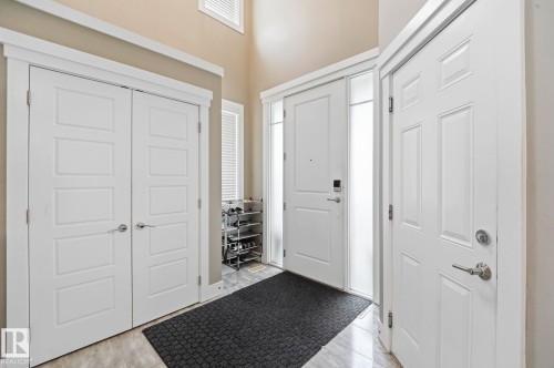 Foyer featuring light gray tile flooring, a tall vaulted ceiling, white paneled doors with chrome hardware, and an entryway door with side-light windows - 1051 174 Street Sw, Edmonton, AB - Indoor Photo Showing Other Room