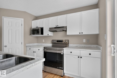 Kitchen featuring white cabinetry with black hardware, stainless steel appliances, and wood-finish flooring - 8923 173 Avenue Nw, Edmonton, AB - Indoor Photo Showing Kitchen With Double Sink