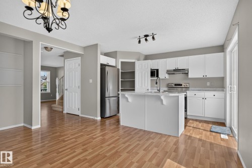 Open-concept living area featuring wood-finish flooring, a contemporary kitchen, white cabinetry, a stainless steel refrigerator, and a sliding glass door - 8923 173 Avenue Nw, Edmonton, AB - Indoor Photo Showing Kitchen With Stainless Steel Kitchen