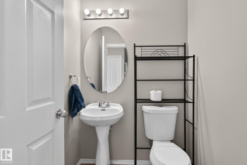 Pedestal sink with chrome faucet, oval wall-mounted mirror, and vanity lighting fixture - 8923 173 Avenue Nw, Edmonton, AB - Indoor Photo Showing Bathroom