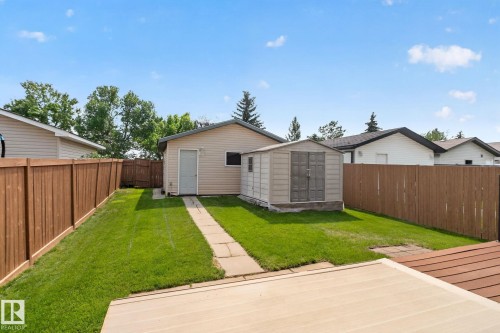 Expansive backyard featuring a manicured lawn, a detached garage with vinyl siding, and a separate storage shed - 8923 173 Avenue Nw, Edmonton, AB - Outdoor