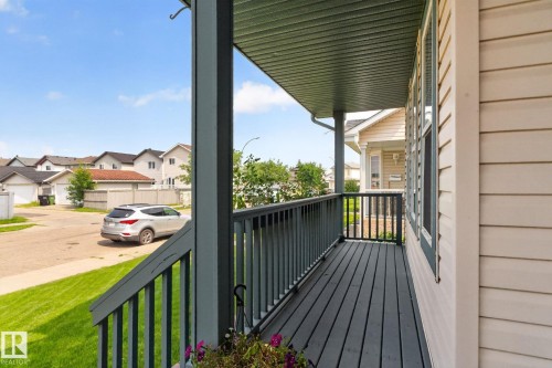 Inviting covered porch with dark wood-finish decking and railing, light-colored siding, and white window trim - 8923 173 Avenue Nw, Edmonton, AB - Outdoor With Exterior
