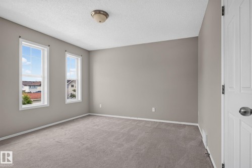 Room featuring two vertical windows with white trim, neutral wall paint, gray carpet flooring, a white paneled door, and a flush mount ceiling light fixture - 8923 173 Avenue Nw, Edmonton, AB - Indoor Photo Showing Other Room
