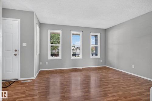 Spacious room featuring wood-finish flooring, light grey painted walls, white baseboards, and a white entry door - 8923 173 Avenue Nw, Edmonton, AB - Indoor Photo Showing Other Room