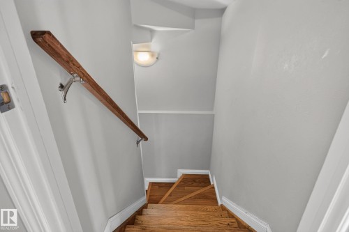 Stairwell featuring wood-finish treads, a wood handrail with chrome brackets, light gray wall paint, white trim, and a wall-mounted light fixture - 8923 173 Avenue Nw, Edmonton, AB - Indoor Photo Showing Other Room