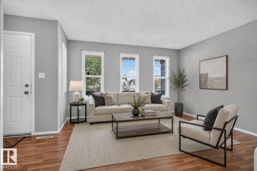 Spacious living area featuring wood-finish flooring, light gray wall paint, and three large windows - 8923 173 Avenue Nw, Edmonton, AB - Indoor Photo Showing Living Room
