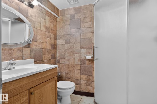Bathroom featuring textured wall tiling, a vanity with wood-finish cabinetry and a white countertop, a toilet, and a shower enclosure with frosted glass doors - 8923 173 Avenue Nw, Edmonton, AB - Indoor Photo Showing Bathroom