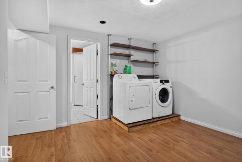 Laundry area featuring wood-finish flooring, light grey wall paint, and overhead shelving - 8923 173 Avenue Nw, Edmonton, AB - Indoor Photo Showing Laundry Room