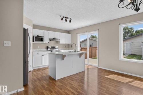 Kitchen featuring a central island with an integrated sink, white cabinetry, stainless steel appliances, and light-toned countertops - 8923 173 Avenue Nw, Edmonton, AB - Indoor Photo Showing Kitchen With Upgraded Kitchen