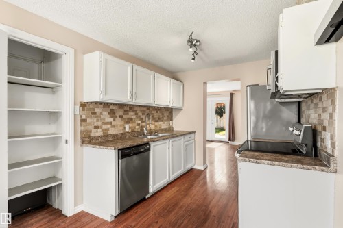 Kitchen featuring wood-finish flooring, white cabinetry, and stone-look countertops with a mosaic tile backsplash - 281 Vantage Lane, Sherwood Park, AB - Indoor Photo Showing Kitchen