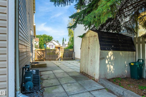 Paved side yard with a wooden storage shed, fenced perimeter, and mature trees - 281 Vantage Lane, Sherwood Park, AB - Outdoor