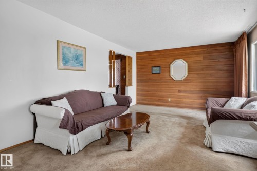 Living area featuring wood paneling, carpeted flooring, white painted walls, and a window with brown drapery - 6012 145 Avenue Nw, Edmonton, AB - Indoor Photo Showing Living Room