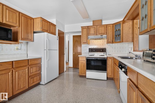 Kitchen featuring wood cabinetry, white countertops, textured backsplash, and stone-finish flooring - 6012 145 Avenue Nw, Edmonton, AB - Indoor Photo Showing Kitchen With Double Sink