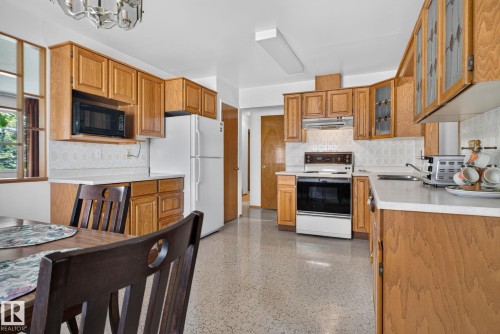 Kitchen featuring wood cabinetry, white countertops, textured backsplash, and light-toned flooring - 6012 145 Avenue Nw, Edmonton, AB - Indoor Photo Showing Kitchen
