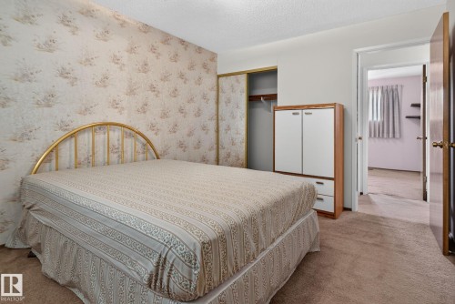 Bedroom featuring patterned wallpaper, neutral carpeting, and a built-in closet with sliding doors - 6012 145 Avenue Nw, Edmonton, AB - Indoor Photo Showing Bedroom