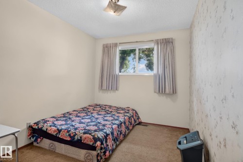 Carpeted room featuring a single window with curtains, textured ceiling, and a flush-mount light fixture - 6012 145 Avenue Nw, Edmonton, AB - Indoor Photo Showing Bedroom