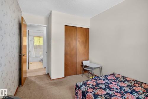 Carpeted room with a textured ceiling, featuring a solid wood bi-fold closet door and a light-colored wall - 6012 145 Avenue Nw, Edmonton, AB - Indoor Photo Showing Bedroom