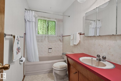 Bathroom featuring a built-in bathtub with shower surround, a window, a vanity with a red countertop and inset sink, a mirrored medicine cabinet, and a toilet - 6012 145 Avenue Nw, Edmonton, AB - Indoor Photo Showing Bathroom