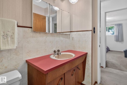 Bathroom vanity featuring a coral countertop, integrated sink, and wood-finish cabinetry - 6012 145 Avenue Nw, Edmonton, AB - Indoor Photo Showing Bathroom