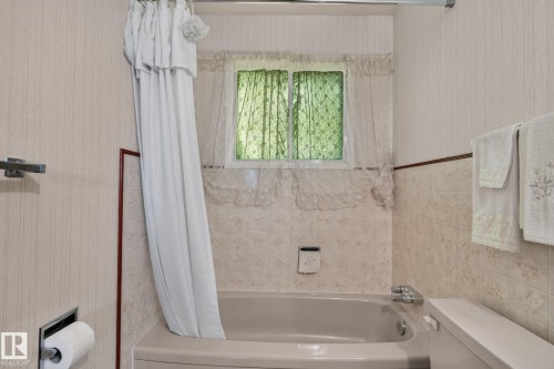 Full-sized bathtub with integrated shower, tiled surround with decorative accent border, and dual-pane window - 6012 145 Avenue Nw, Edmonton, AB - Indoor Photo Showing Bathroom