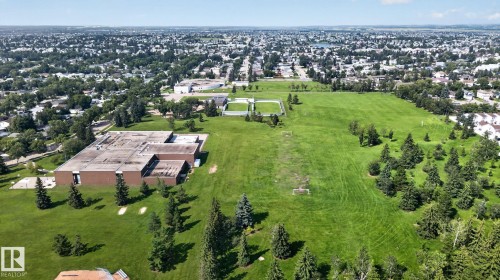 Expansive green space featuring a sprawling grassy field, mature evergreen trees, and a distant urban landscape - 6012 145 Avenue Nw, Edmonton, AB - Outdoor With View