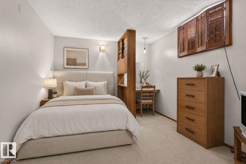 Comfortable bedroom showcasing warm wood-finish furnishings, including a five-drawer dresser and shelving unit with louvered doors - 6012 145 Avenue Nw, Edmonton, AB - Indoor Photo Showing Bedroom
