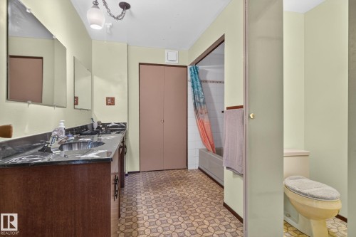 Bathroom featuring a double vanity with dark countertops and dual sinks, patterned floor tiles, and a built-in bathtub with white tile surround - 6012 145 Avenue Nw, Edmonton, AB - Indoor
