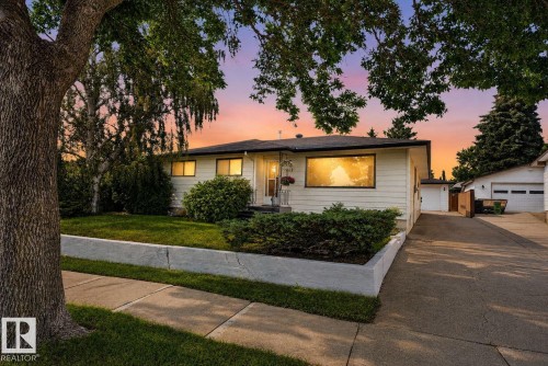 Exterior featuring white siding, a contrasting dark roof, and a mature tree with established landscaping - 6012 145 Avenue Nw, Edmonton, AB - Outdoor