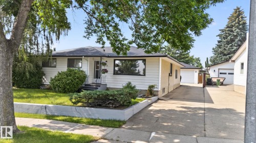 White siding exterior with dark trim windows, front yard landscaping, concrete driveway, and detached garage - 6012 145 Avenue Nw, Edmonton, AB - Outdoor