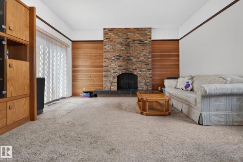 Living area featuring a brick fireplace with an arched firebox, wood paneling, light-toned carpeting, and a built-in wood cabinetry unit - 6012 145 Avenue Nw, Edmonton, AB - Indoor Photo Showing Living Room With Fireplace