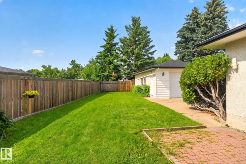Expansive rear yard featuring a wooden privacy fence, a detached garage with a white overhead door, and a concrete driveway - 6012 145 Avenue Nw, Edmonton, AB - Outdoor