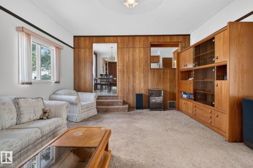Warm wood-paneled wall with a built-in entertainment center featuring glass-front cabinets and lower drawers - 6012 145 Avenue Nw, Edmonton, AB - Indoor Photo Showing Living Room