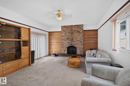Spacious living area featuring a brick-surround fireplace, wood paneling, and wall-to-wall carpeting - 6012 145 Avenue Nw, Edmonton, AB - Indoor Photo Showing Living Room With Fireplace