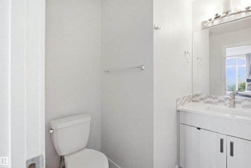 White bathroom vanity with dual-door cabinetry, a white countertop, and a tiled backsplash - #22 723 172 Street Sw, Edmonton, AB - Indoor Photo Showing Bathroom