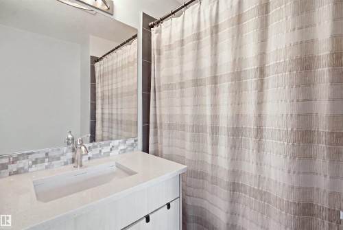 Bathroom featuring a white vanity with integrated sink, a solid surface countertop, and a mosaic tile backsplash - #22 723 172 Street Sw, Edmonton, AB - Indoor Photo Showing Bathroom