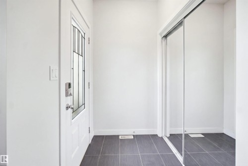 Entryway featuring a white door with decorative glass inserts, a digital lock, and a sliding mirrored closet door - #22 723 172 Street Sw, Edmonton, AB - Indoor Photo Showing Other Room